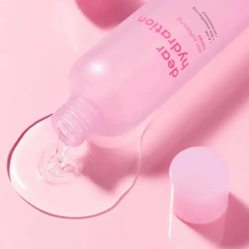 Rosa Flasche, Flüssigkeit wird ausgegossen. Text: "dear hydration", "skin softening toner", "A-HA", "pH balanced". Marke: BANILA CO.