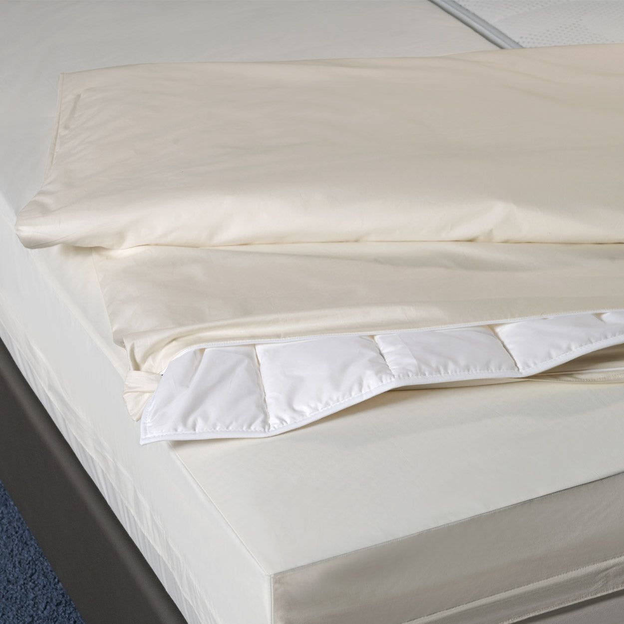 Beige Bettdecken-Encasings auf einem Bett. Der untere Teil ist mit Steppnähten versehen.