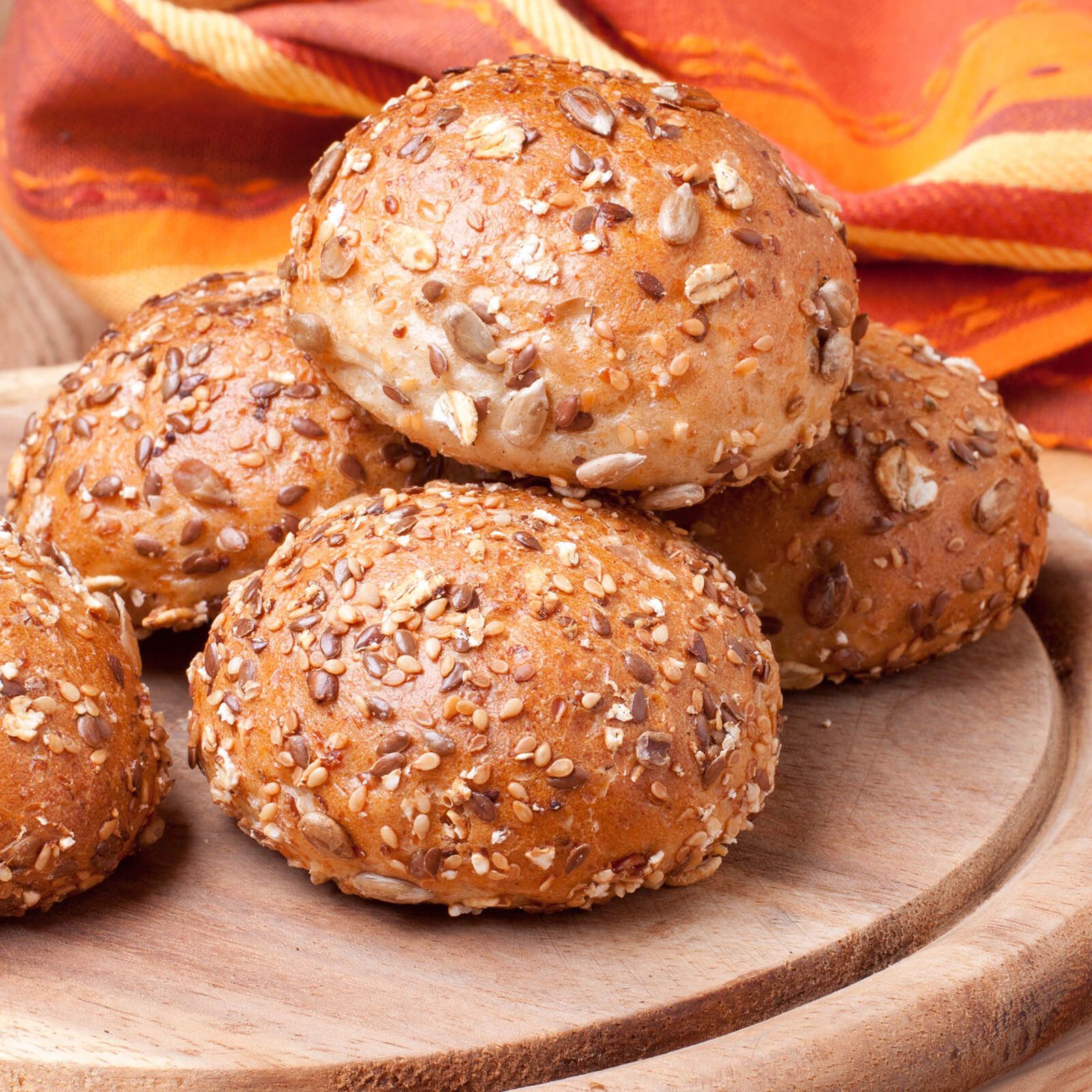 Mehrere Brötchen auf einem Holzbrett. Brötchen mit Körnern und Samen. Holzbrett im Vordergrund, Hintergrund unscharf.