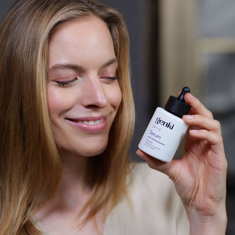 Frau hält Genki Serum-Flasche. Flasche mit schwarzem Deckel und Pipette. Frau lächelt.