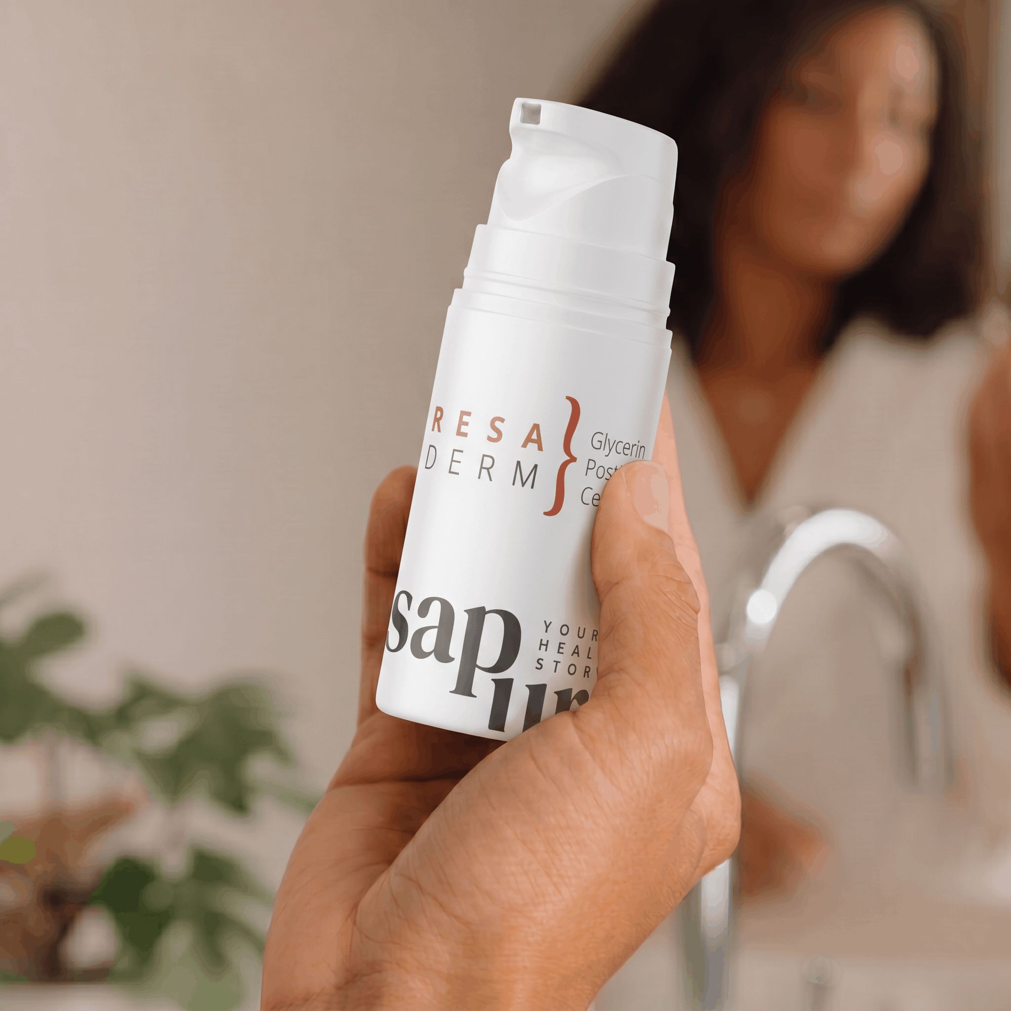 Hand hält weiße Pumpflasche mit Rosacea Creme vor einem Badezimmerspiegel.