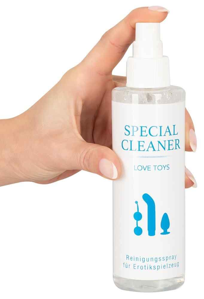 Hand hält eine Flasche Reinigungsspray. Aufdruck: "SPECIAL CLEANER", "LOVE TOYS" und Illustrationen. Sprühkopf. Transparente Flüssigkeit sichtbar.