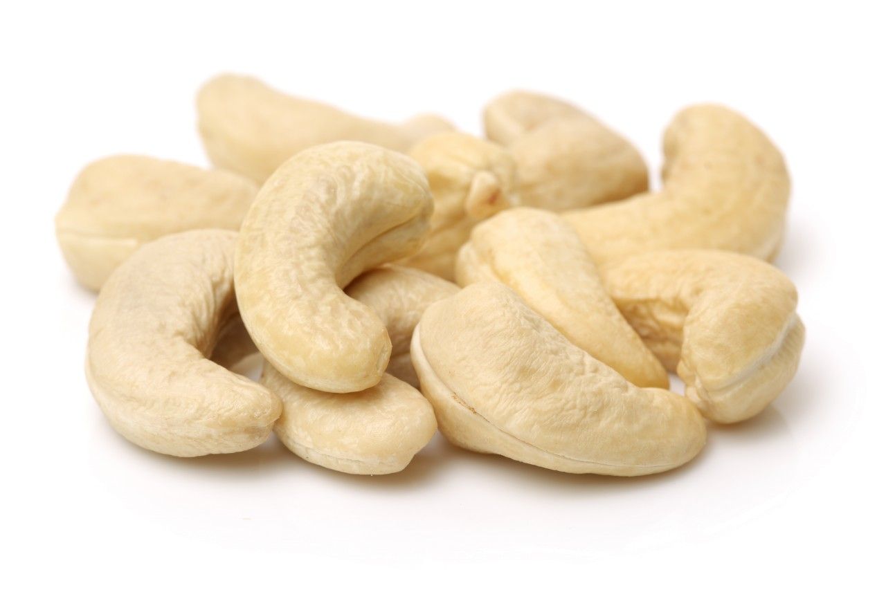 Haufen Cashewkerne, hellbraun, auf weißem Hintergrund. Einzelne Kerne sind gebogen und bohnenförmig.
