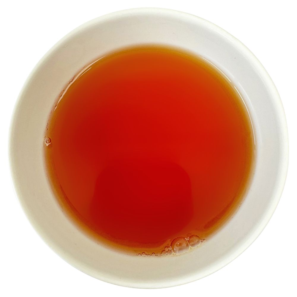Runder, weißer Becher mit rotem Tee. Der Tee hat Blasen an der Oberfläche.