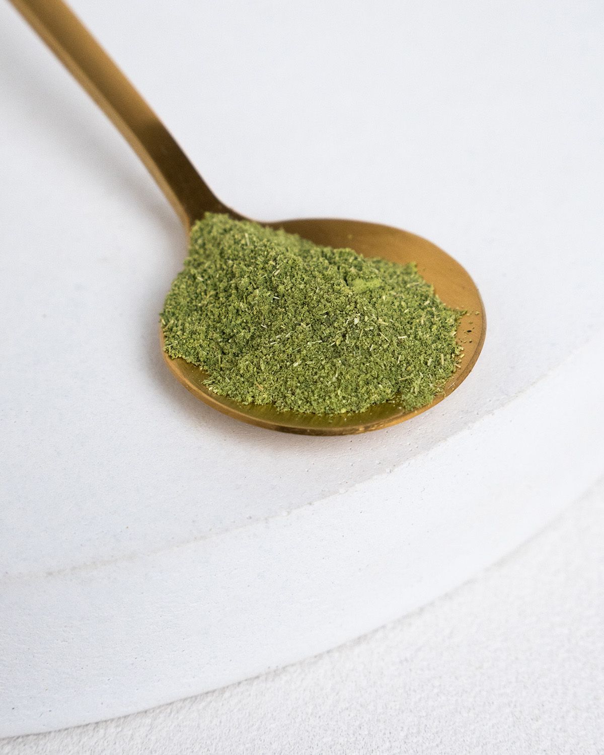 Goldener Löffel mit grünem Moringa-Pulver. Auf weißem Hintergrund.