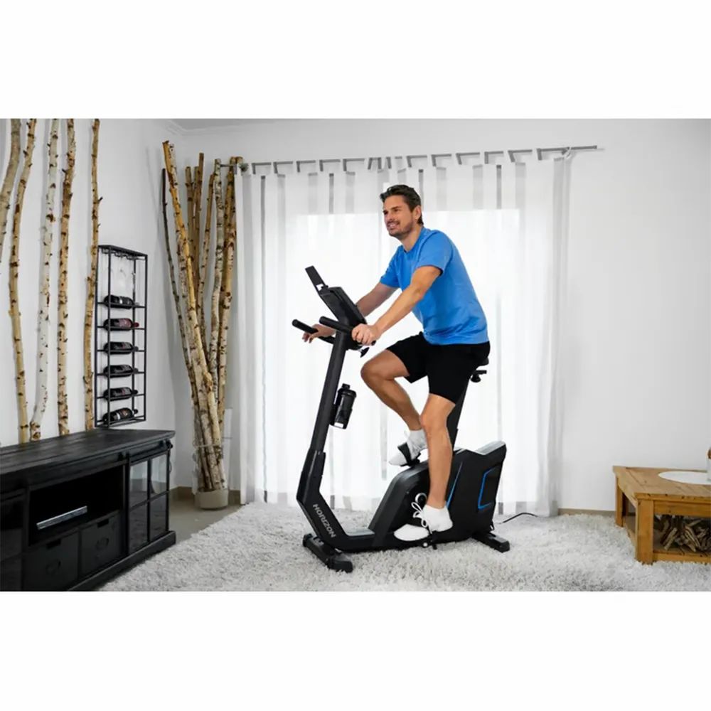Mann auf Ergometer Horizon Fitness 5.0Ui. In Wohnraum. Mit Display, Pedalen, Sattel und Getränkehalter.