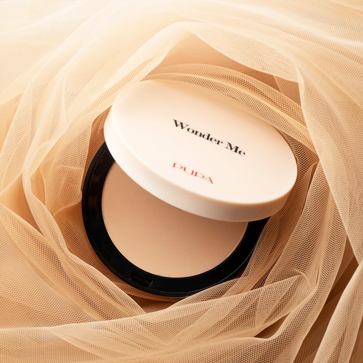Offener Puderbehälter. Deckel mit "Wonder Me" und "PUPA". Auf beigem Stoff. Beige Puder.
