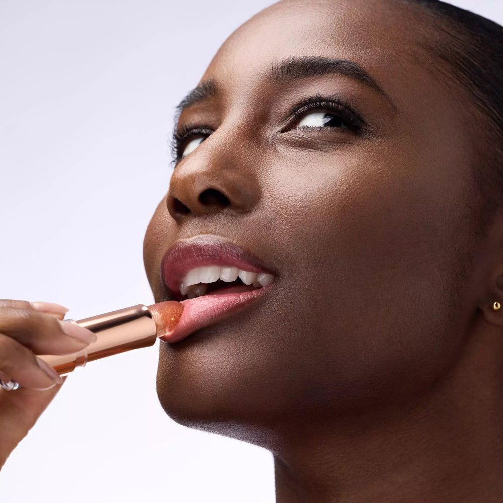 Dunkelhäutige Frau trägt Lippenbalsam auf. Roségoldene Hülse. Lippen glänzen.