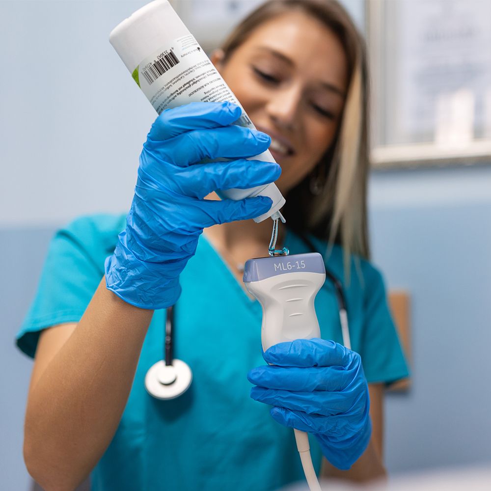 Person in blauen Handschuhen trägt Ultraschallgel auf einen Schallkopf auf.