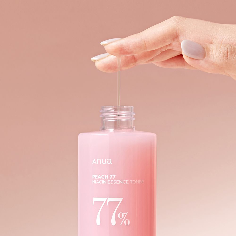 Eine Hand tropft ANUA Peach 77% Niacin Essence Toner aus einer Flasche.