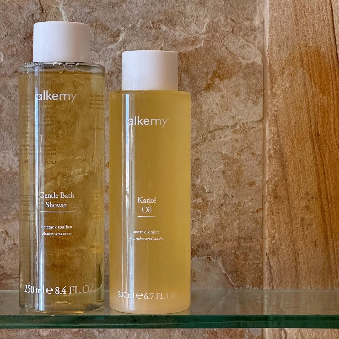Zwei Alkemy-Flaschen: Duschgel (250ml) und Karité-Öl (200ml) auf einem Regal.
