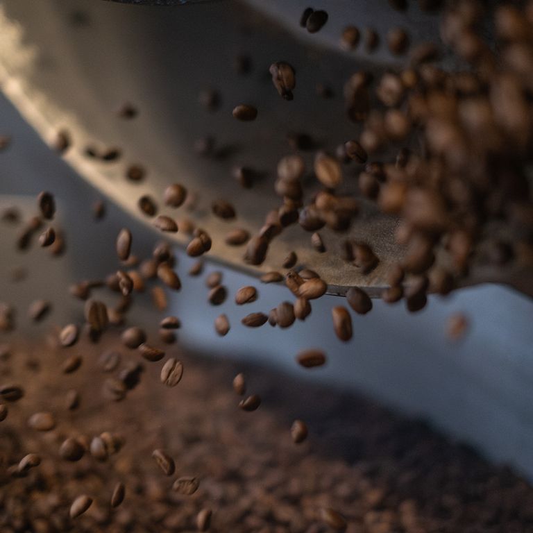 Kaffeebohnen fallen aus einer Metallschale. Braune Kaffeebohnen in Bewegung.