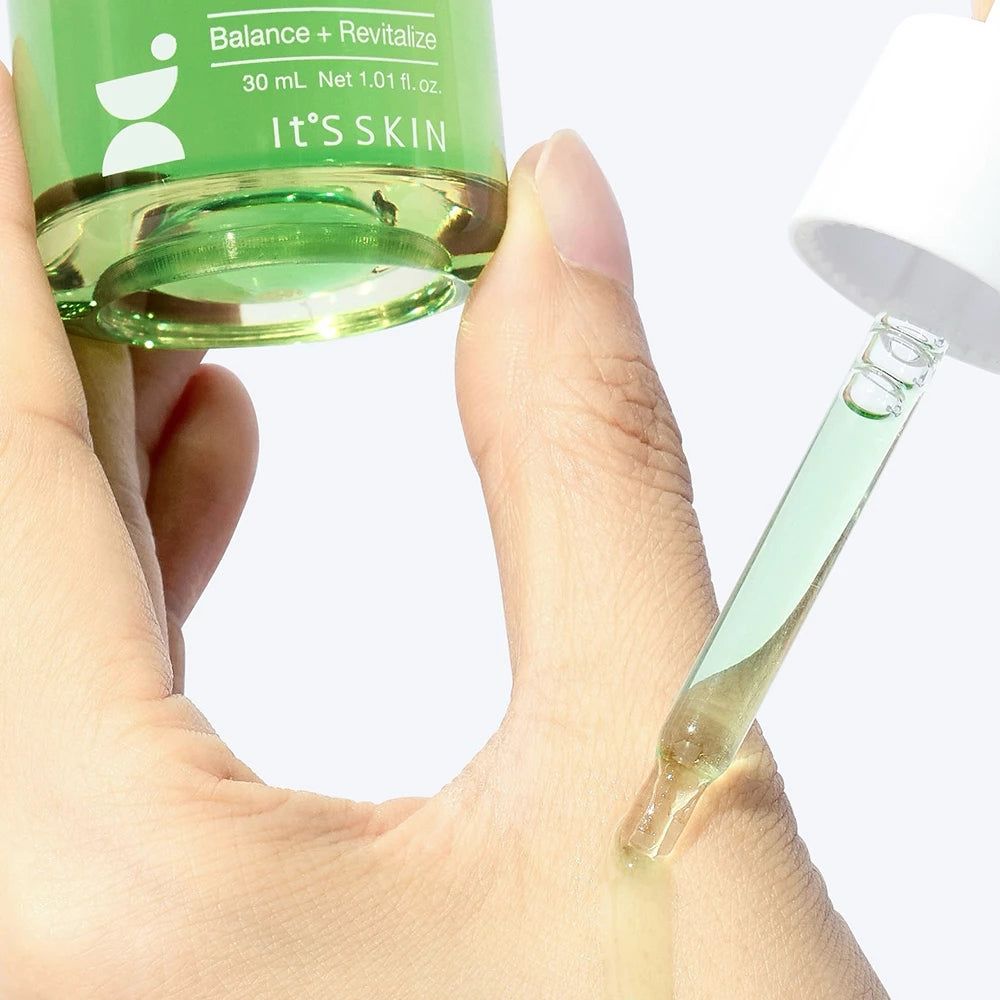 Grüne Flüssigkeit tropft aus Pipette auf eine Hand. Flasche mit 'It's SKIN' und 'Balance + Revitalize' beschriftet.