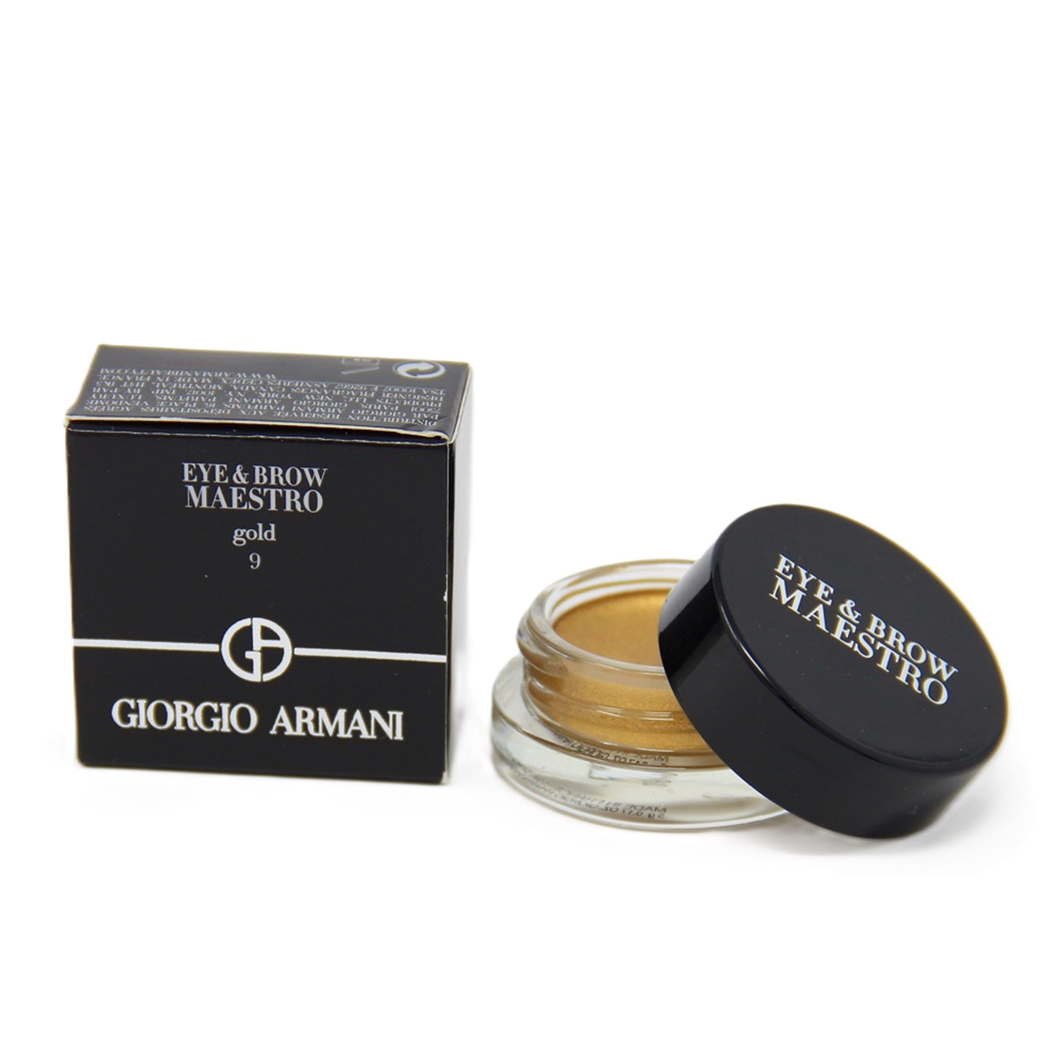 Goldfarbener Lidschatten in einem Glasbehälter mit schwarzem Deckel. Daneben eine schwarze Schachtel mit Produktinformationen und Logo.