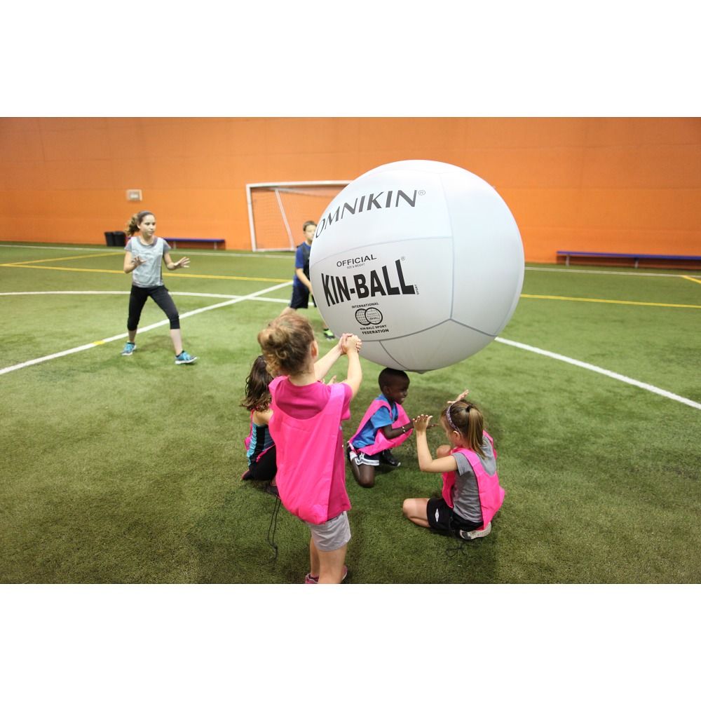 Weißer Kin-Ball. Kinder spielen in einer Sporthalle. Aufschrift: OMNIKIN, OFFICIAL KIN-BALL. Kinder tragen Westen.