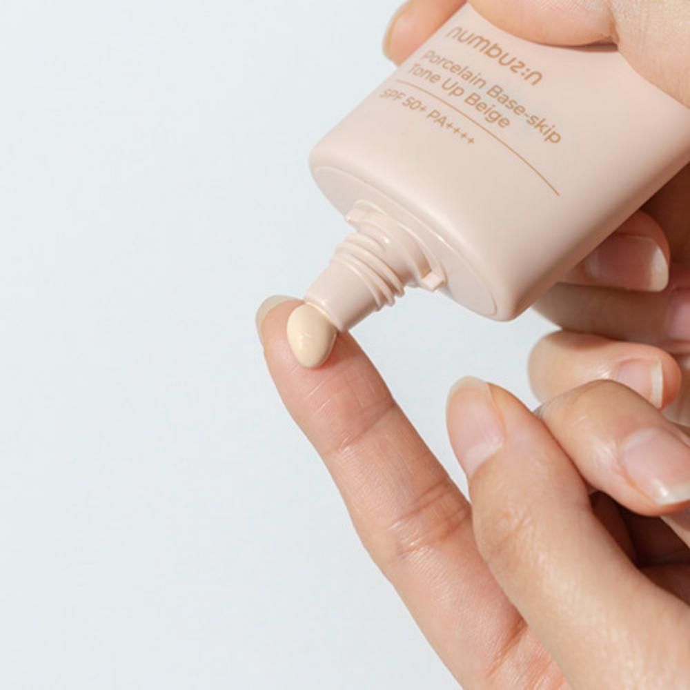 Beigefarbene Creme wird aus einer Tube auf einen Finger gedrückt. Aufschrift: n:umbuz:in, Porcelain Base-skip, Tone Up Beige, SPF 50+ PA++++.