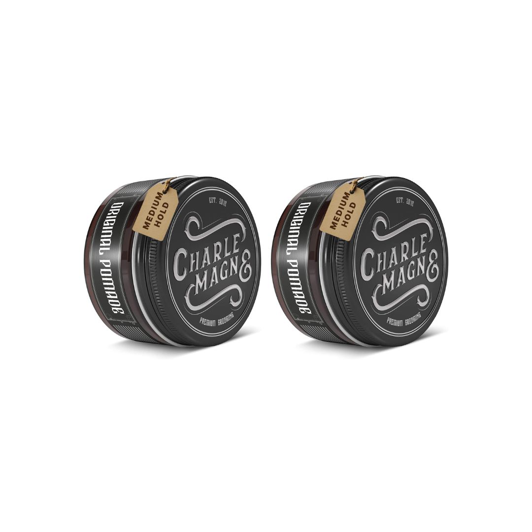 Zwei runde, schwarze Dosen mit Deckel. Auf jeder Dose steht "Charle Magne" und "Original Pomade". An jeder Dose hängt ein Etikett mit "Medium Hold".