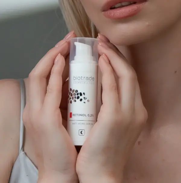 Weißes Serum mit Pumpverschluss. Aufschrift: Biotrade, Retinol 0,2%, Anti-Aging Serum. Mondsymbol. Hände halten es.