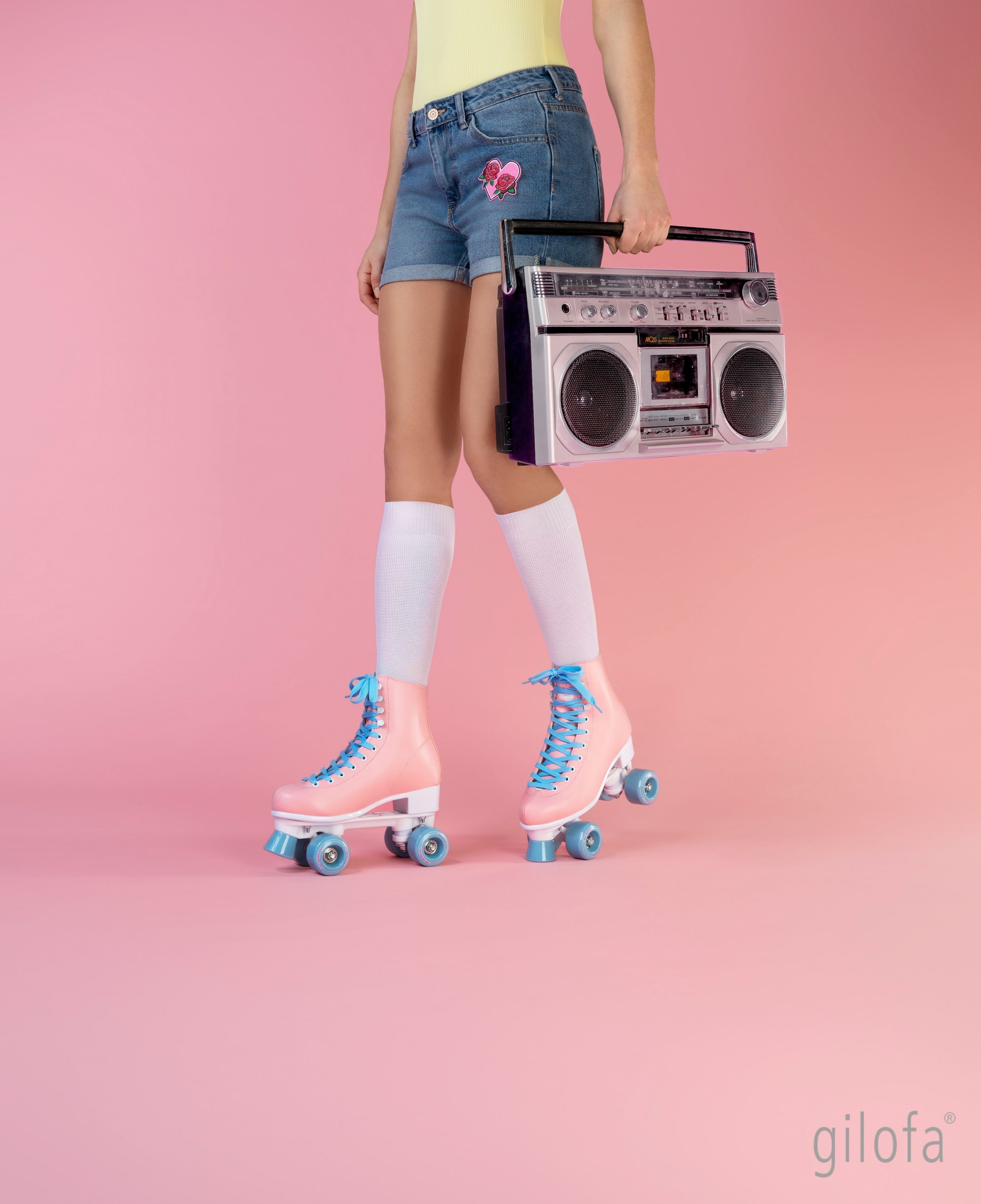 Person mit Rollschuhen und Kniestrümpfen. Rosa Rollschuhe mit blauen Schnürsenkeln. Weiße Kniestrümpfe. Logo 'gilofa'.