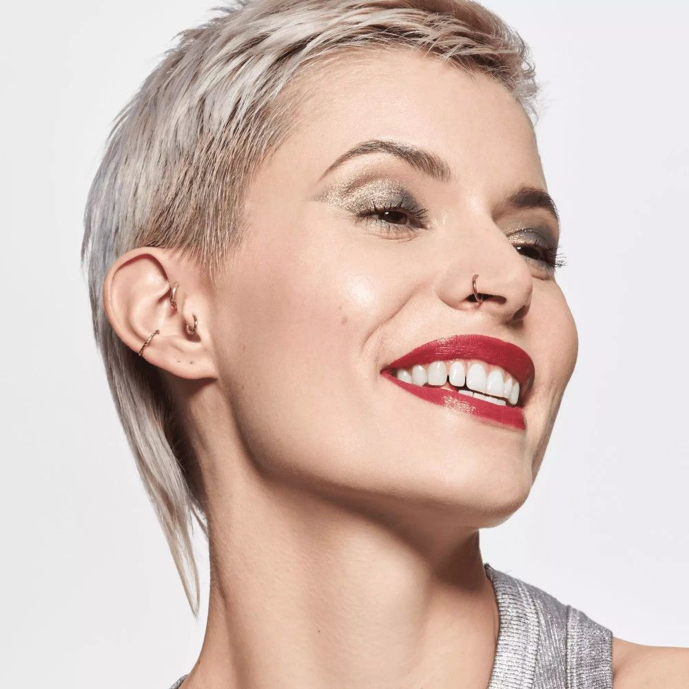 Porträt einer Frau mit silbernem Top und Lidschatten. Sie lächelt und trägt roten Lippenstift.