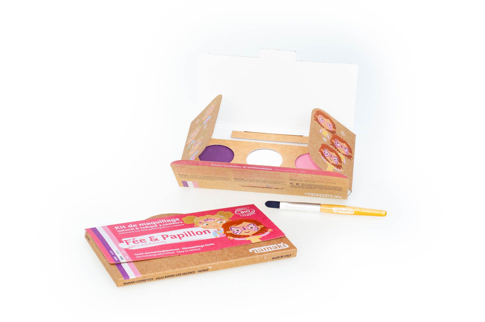 Geöffnete Namaki Bio Schminkset Fee & Schmetterling. Farben rosa, violett und weiß. Pinsel liegt daneben.