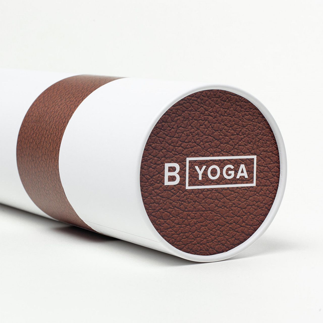 Zylindrische Verpackung, weiß, mit braunem Yogamatten-Ende und Logo "B YOGA".