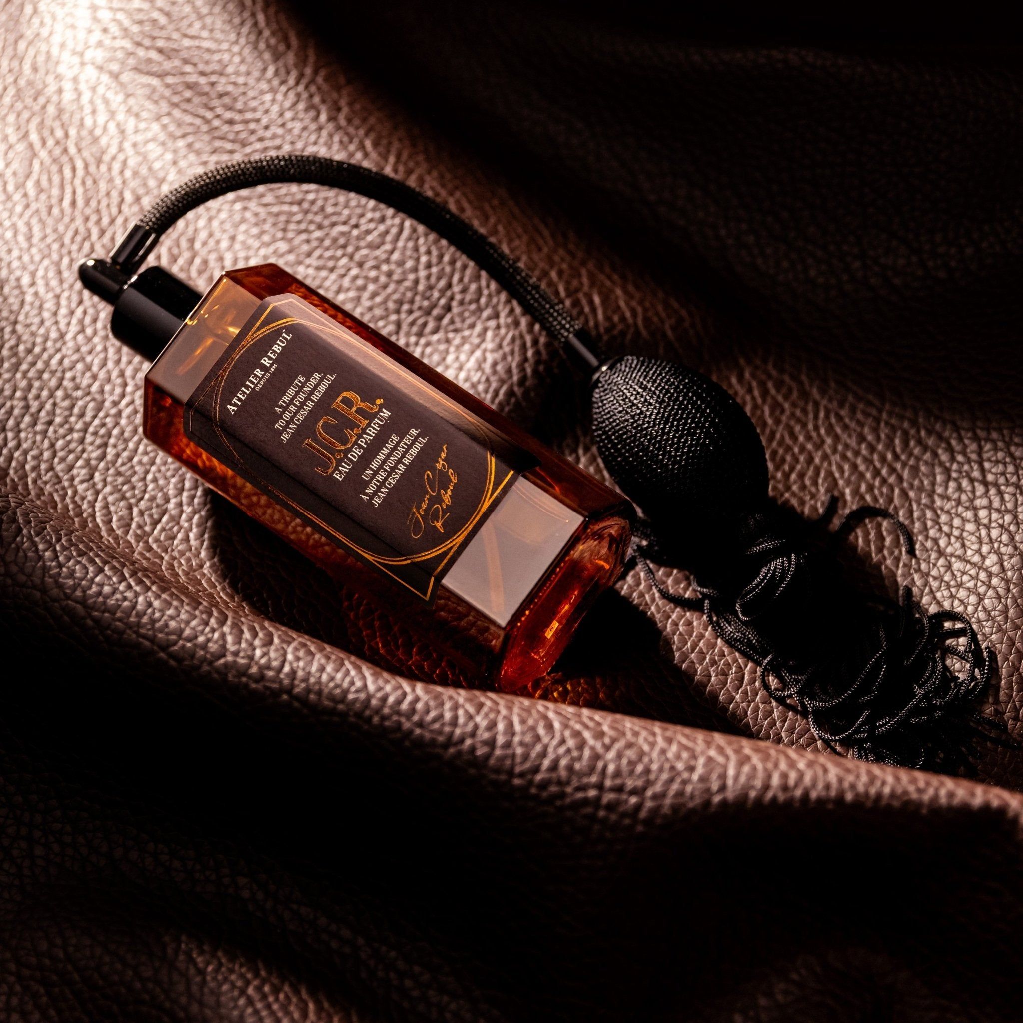 Braune Glasflasche mit schwarzem Zerstäuber und Quaste. Aufschrift: Atelier Rebul J.C.R. Eau de Parfum.