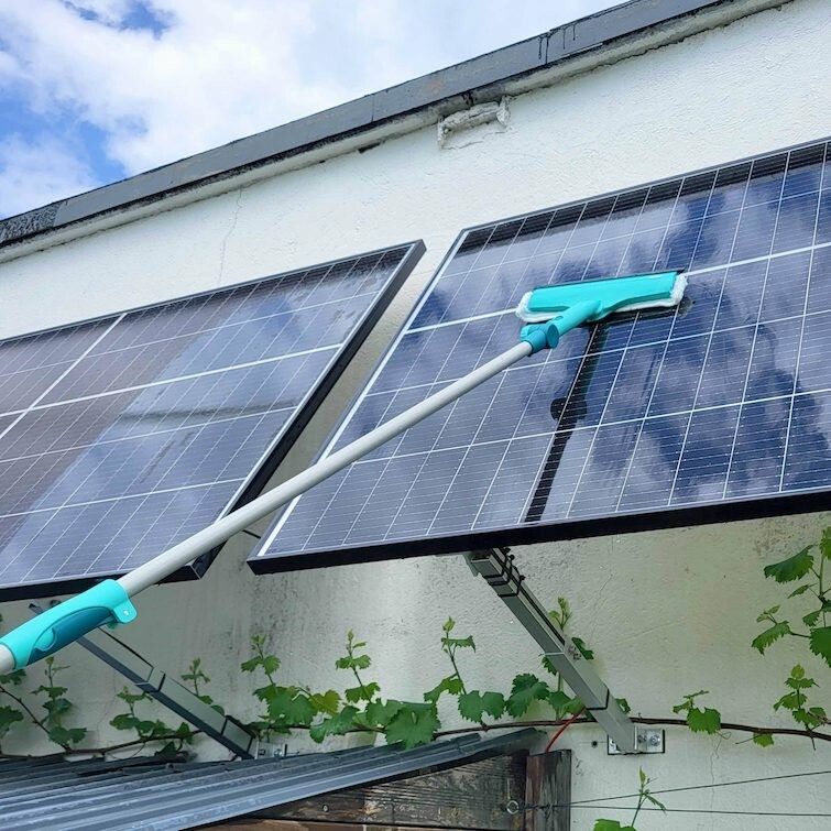 Fensterwischer mit Teleskopstiel reinigt Solarmodule. Türkis-farbener Wischer, grauer Stiel. Anwendung im Freien.