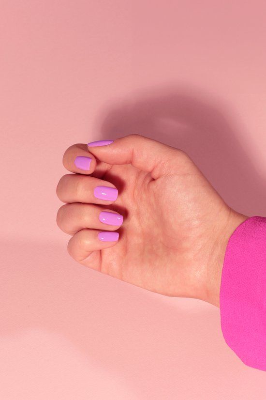 Hand mit lila lackierten Nägeln. Rosa Hintergrund. Ärmel eines pinkfarbenen Oberteils.