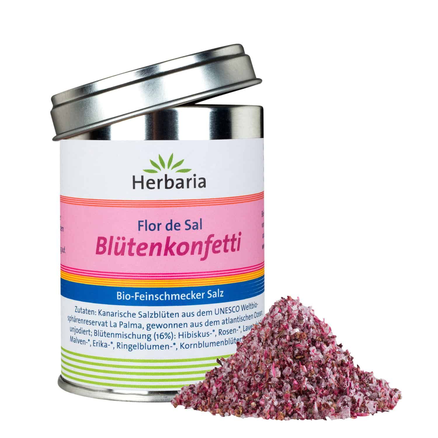 Zylindrische Dose mit Deckel, gefüllt mit Blütenkonfetti. Aufschrift: Herbaria, Flor de Sal Blütenkonfetti. Daneben ein Haufen Blütenkonfetti.