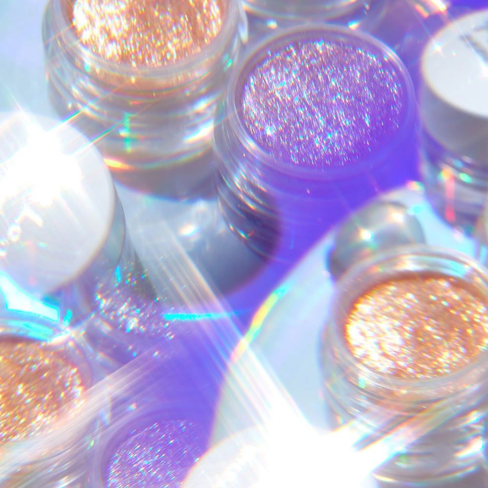 Mehrere kleine Gläser mit schimmerndem Glitzer in Gold- und Lilatönen.