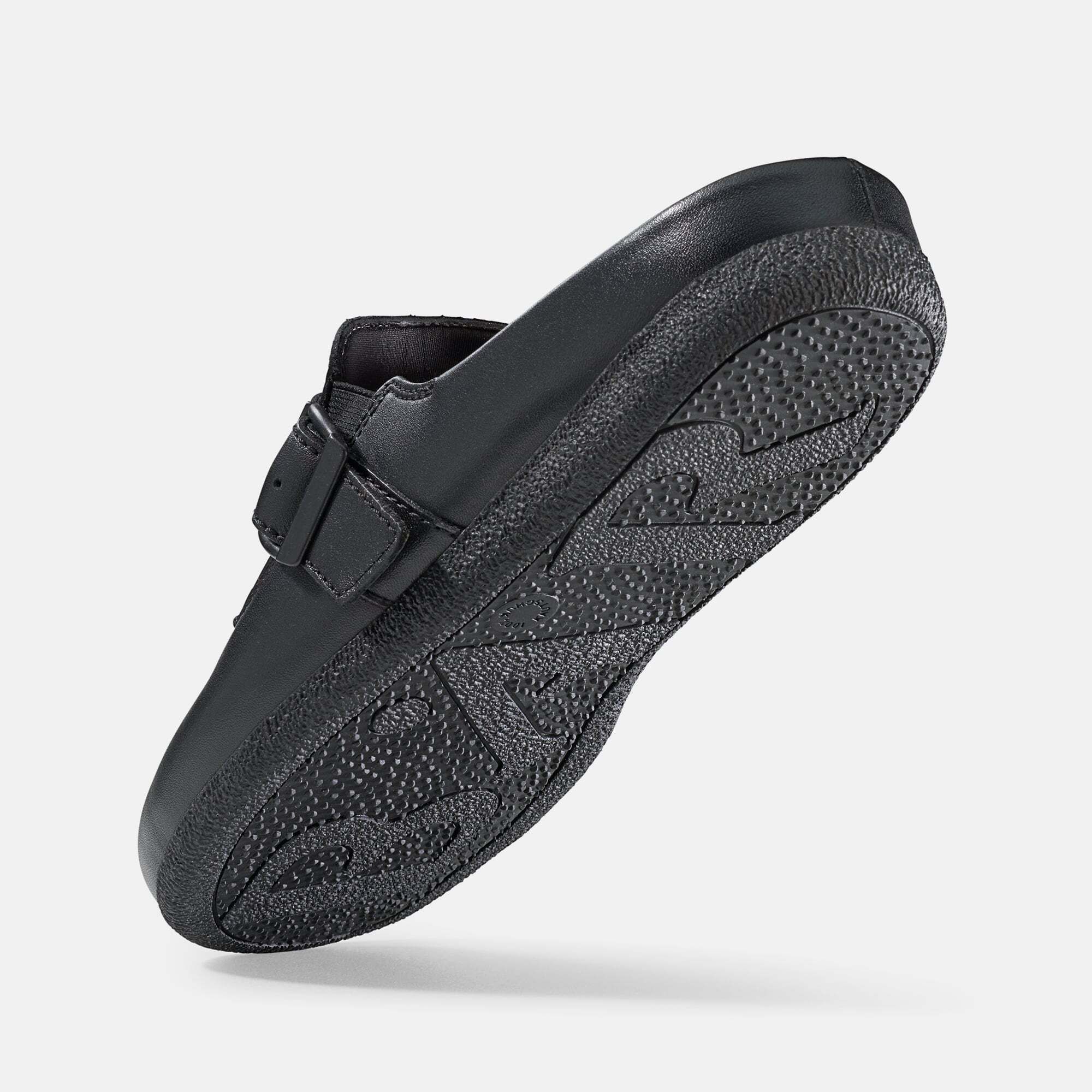 Schwarze Pantolette von unten gesehen. Profilierte Sohle. Riemen mit Schnalle. Schuh leicht schräg gestellt.