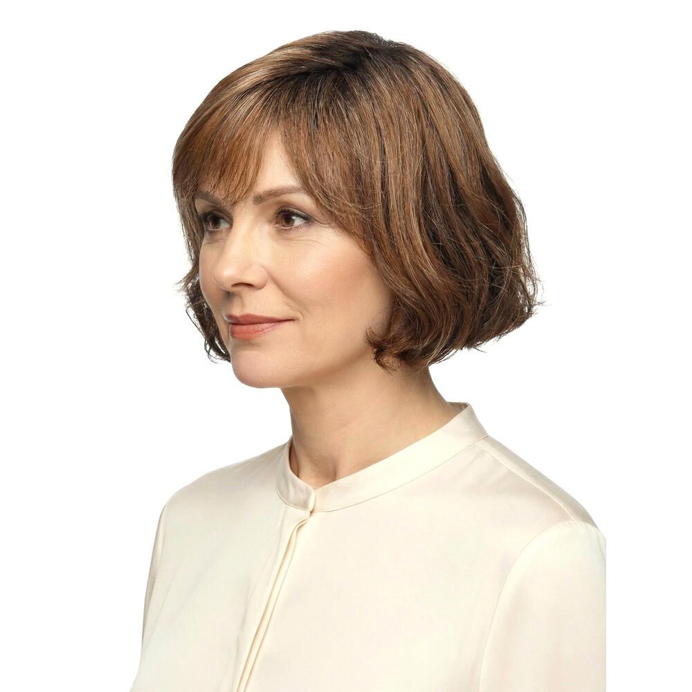 Frau mit brauner Perücke mit Pony. Die Perücke hat blonde Strähnen und welliges Haar. Sie trägt ein weißes Hemd.
