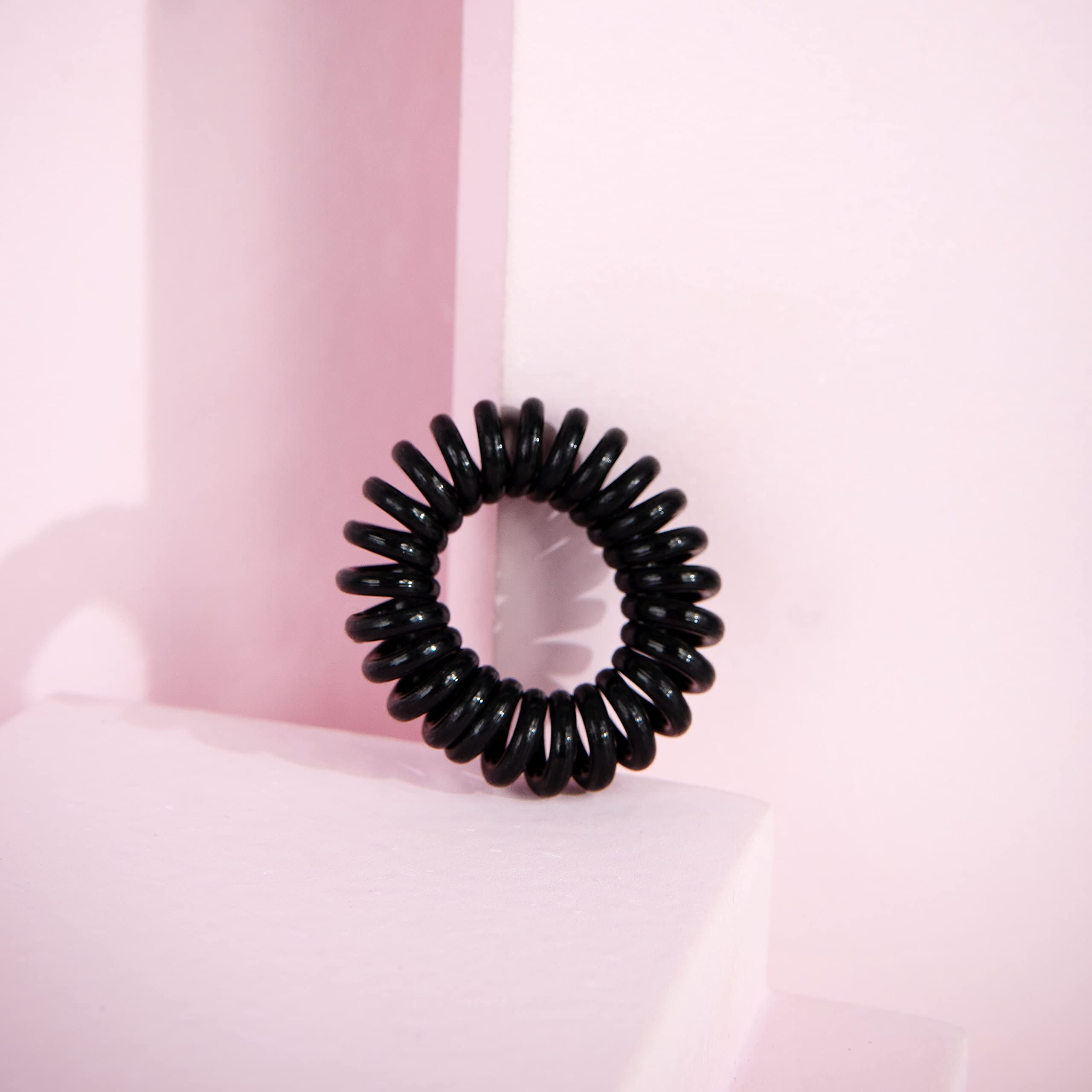 Schwarzes, spiralförmiges Haargummi auf rosa Oberfläche.