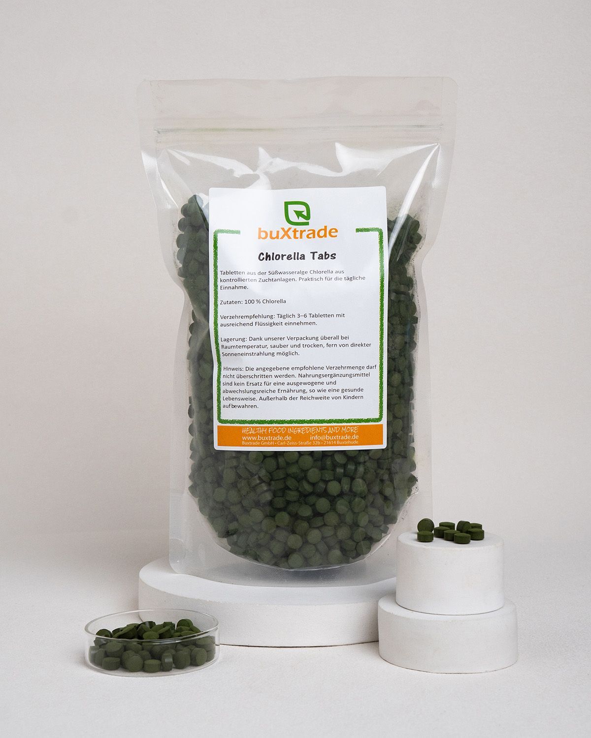 Transparente Tüte mit grünen Tabletten. Aufkleber: buXtrade Chlorella Tabs. Tabletten in Schale.