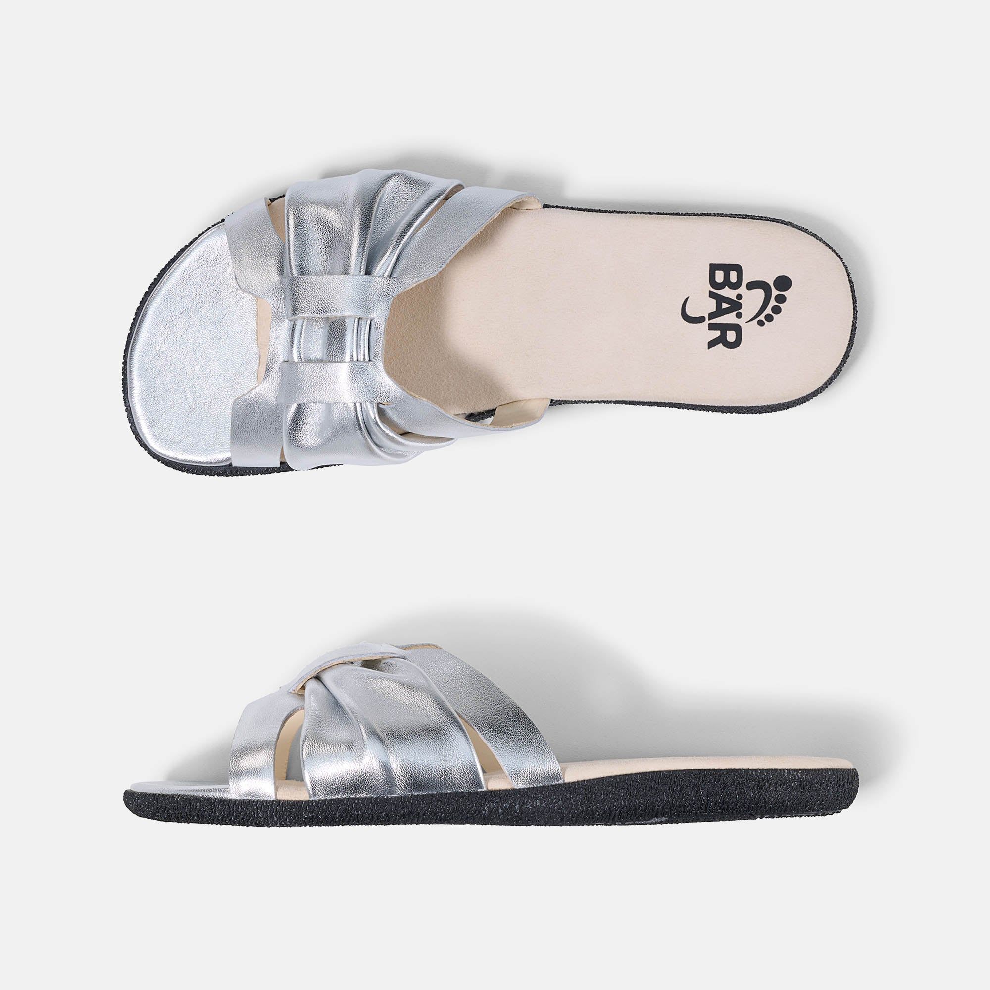 Zwei silberne BÄR Tiana Damen-Pantoletten. Breite Form. Obermaterial mit gekreuzten Riemen. Schwarze Sohle, helle Innensohle mit Logo.