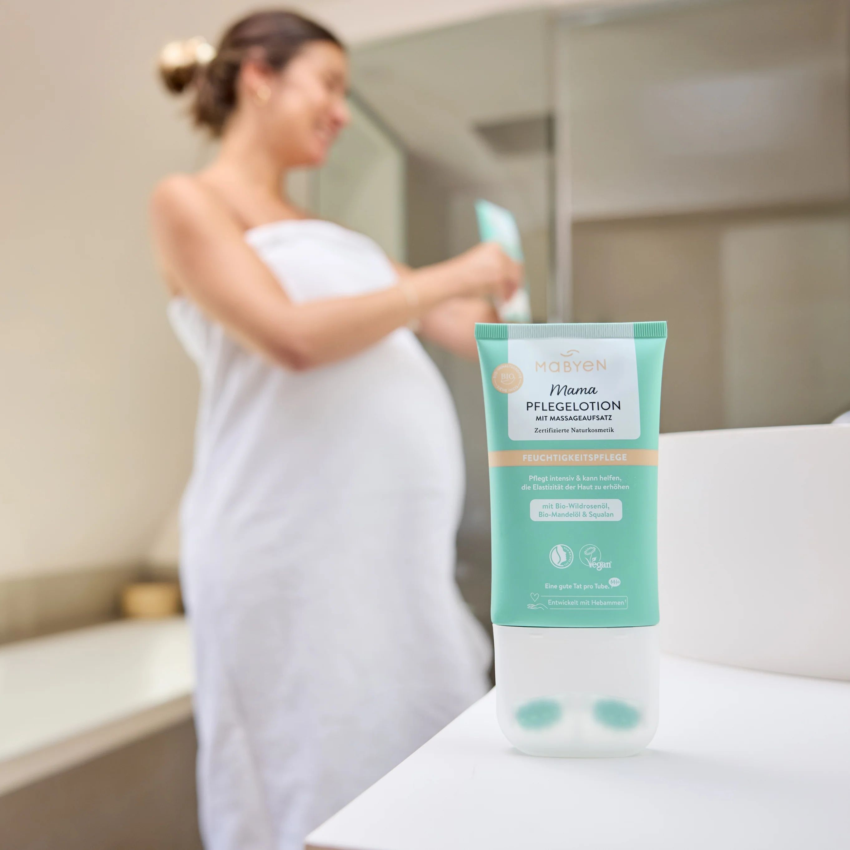 Schwangere Frau im Bad mit MABYEN Pflegelotion Mama. Die Lotion steht auf einer Ablage. Im Hintergrund ein Spiegel und eine Badewanne.