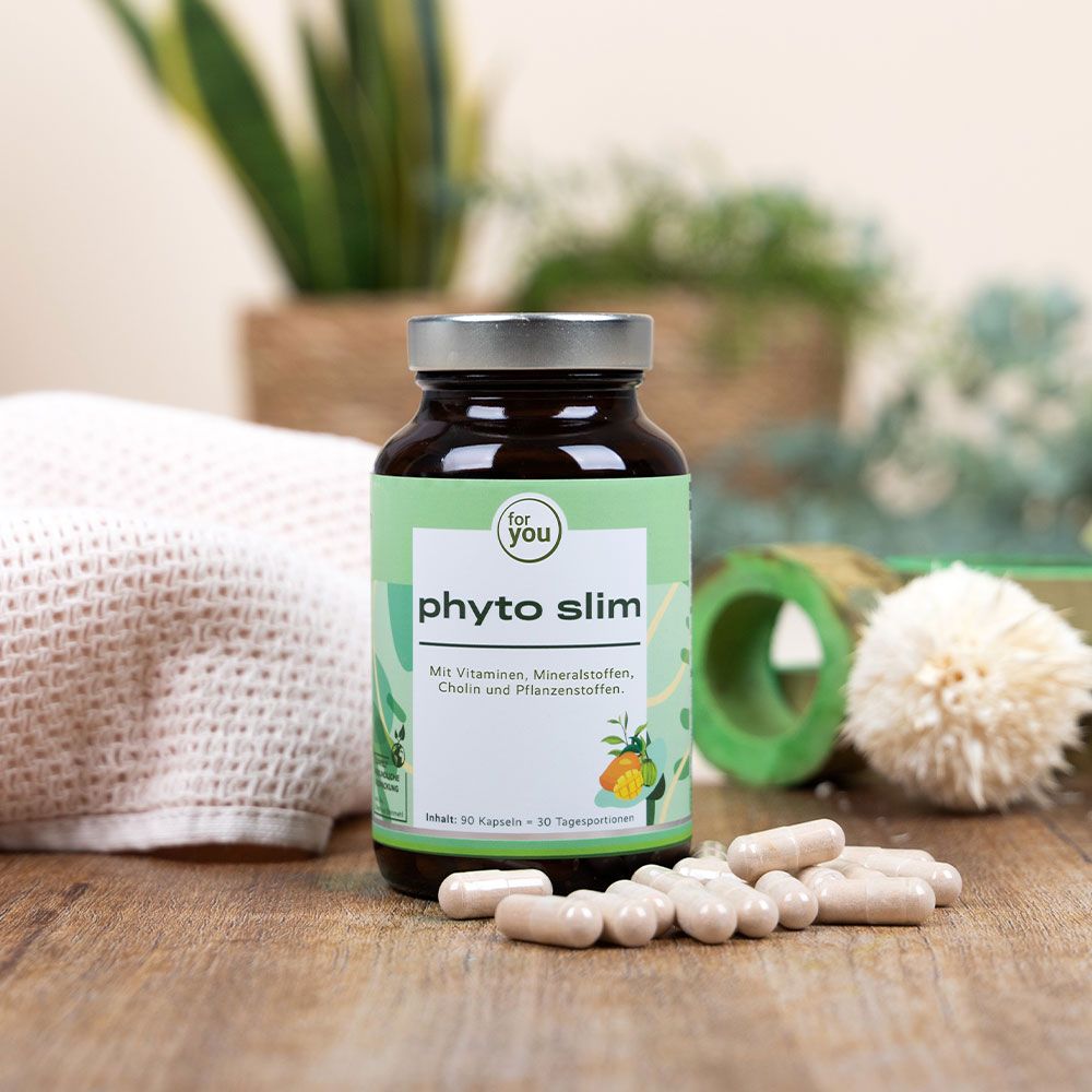 Braune Glasflasche mit grünem Etikett. Aufschrift: Phyto Slim. Daneben Kapseln. Hintergrund: Pflanzen und Textilien.