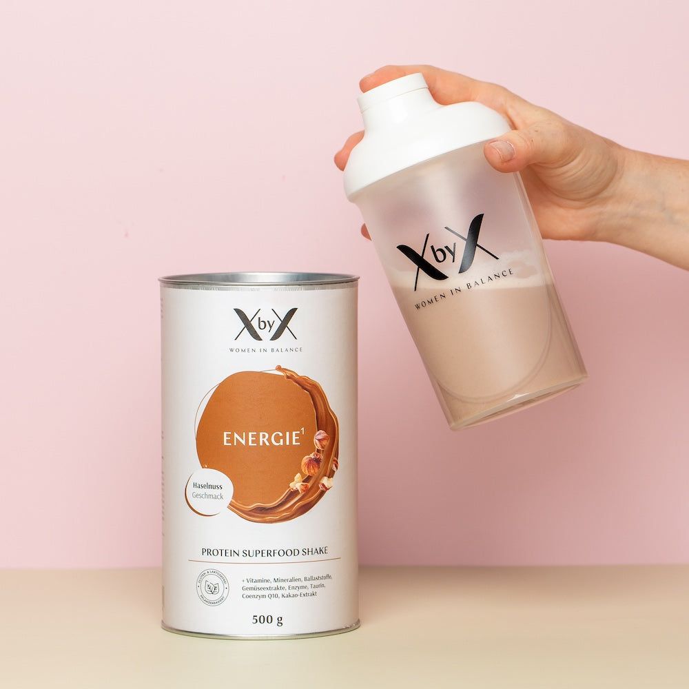 Person hält Shaker mit Getränk. Dose mit 'Energie', 'Protein Superfood Shake'. Rosa Hintergrund.