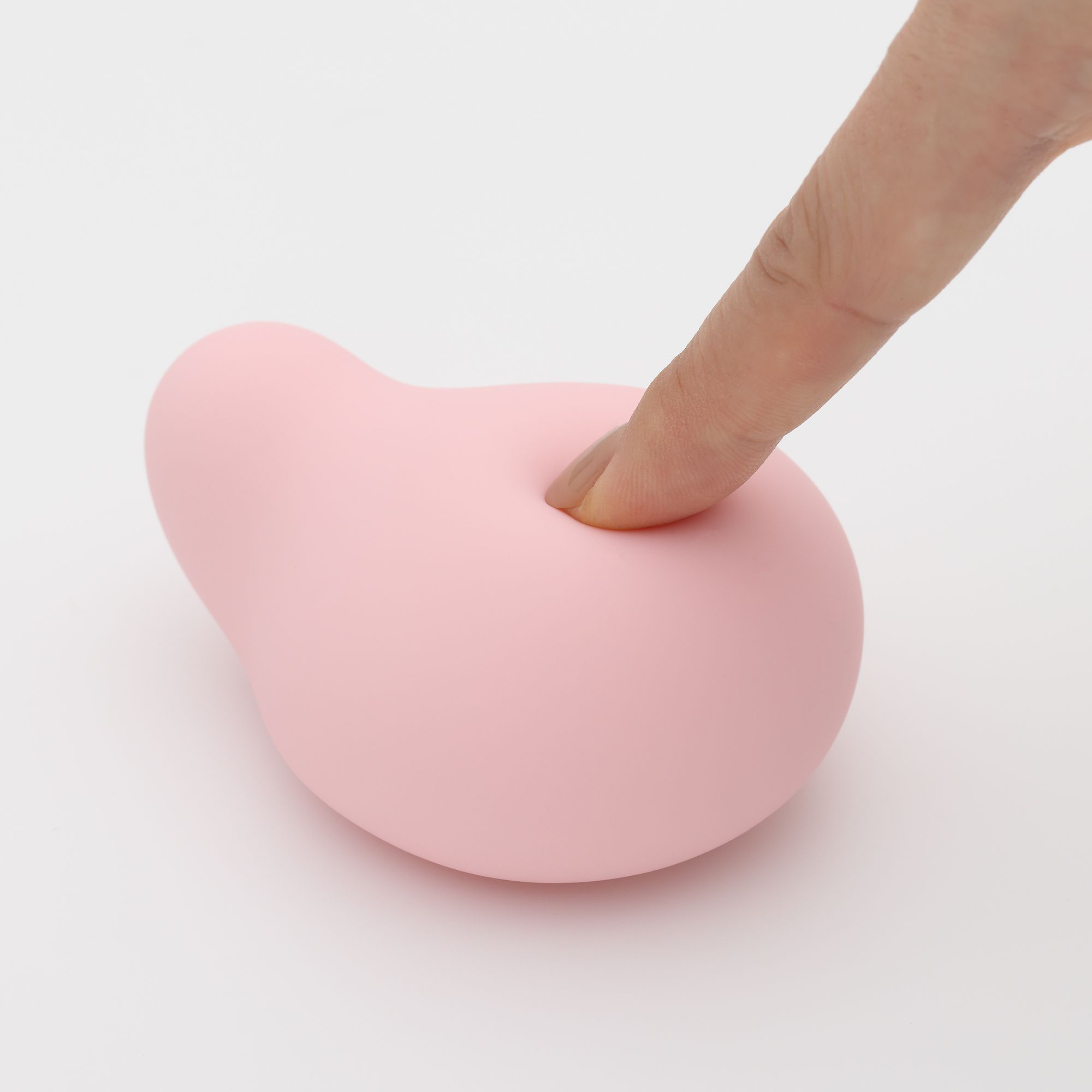 Rosa, tropfenförmiges Produkt. Ein Finger berührt eine Vertiefung. Auf weißem Hintergrund.