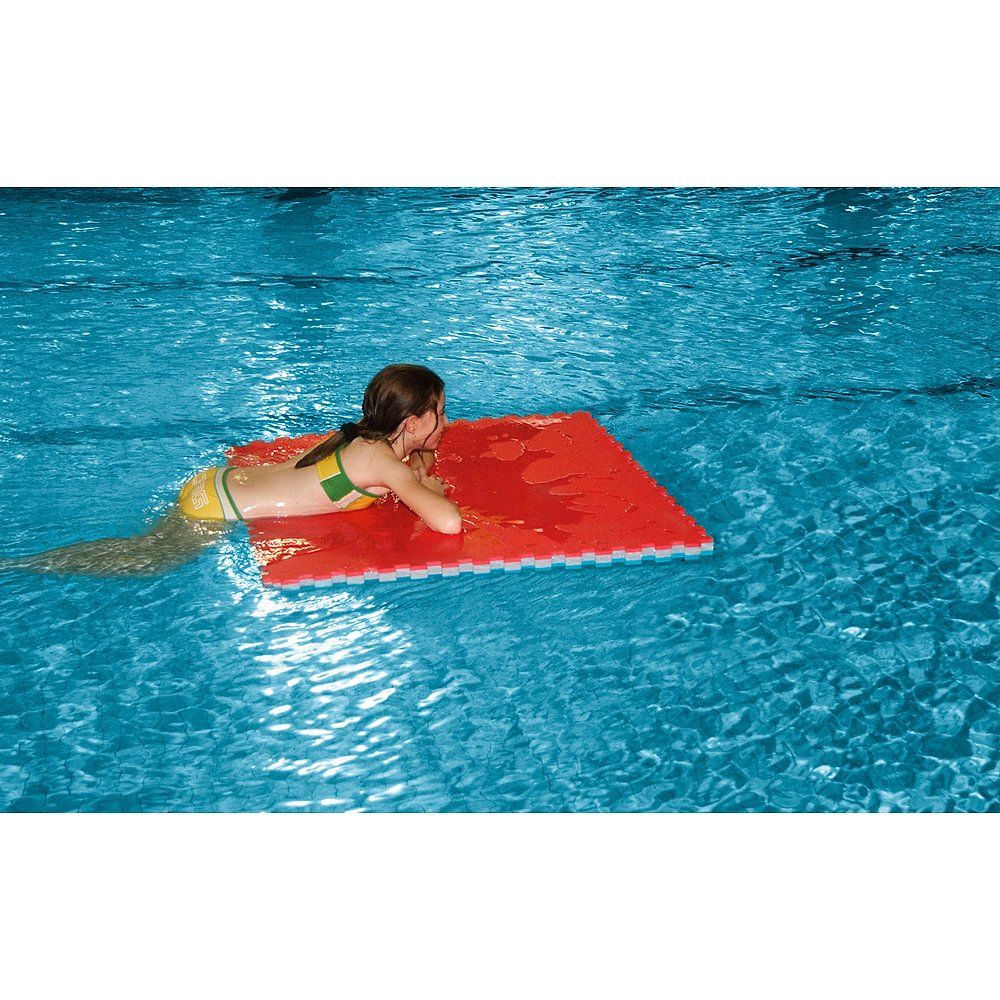 Rote, quadratische Judomatte im Wasser. Ein Mädchen liegt auf der Matte. Die Matte hat ein Puzzle-Design.