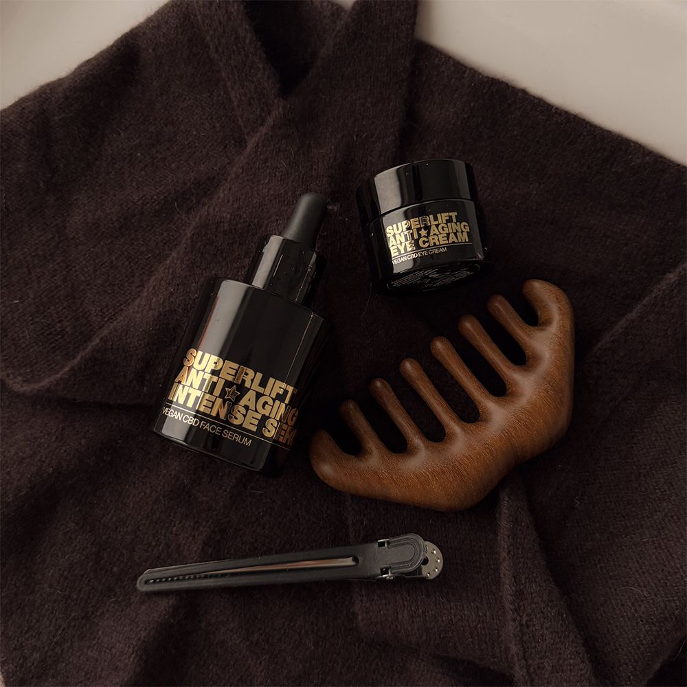 Serumflasche, Augencreme, Kamm und Haarspange auf braunem Tuch. Goldener Text: Superlift.