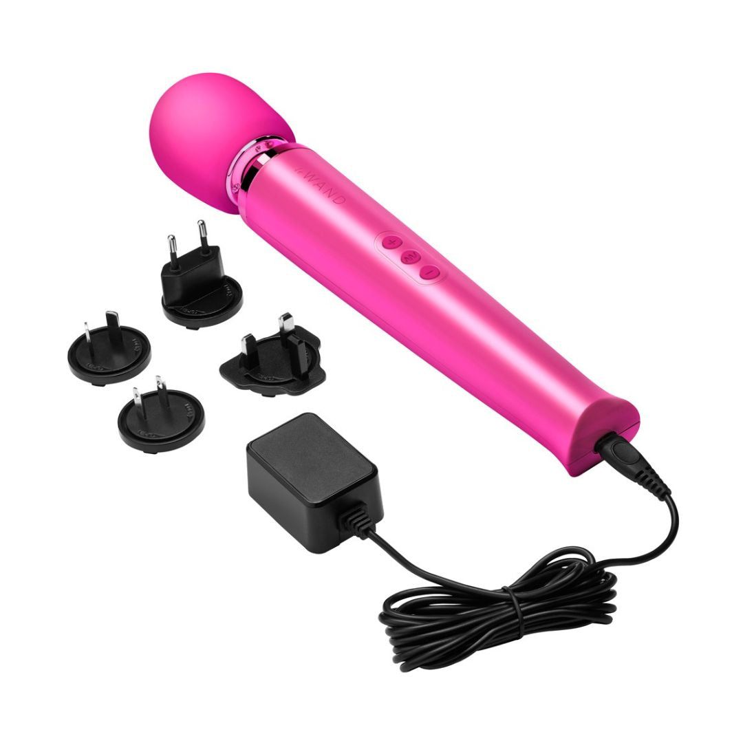 Magenta Massagegerät, Zubehör. Zylindrischer Griff mit drei Knöpfen. Abgerundeter Kopf. Netzkabel, Adapter. Marke "WAND" sichtbar.