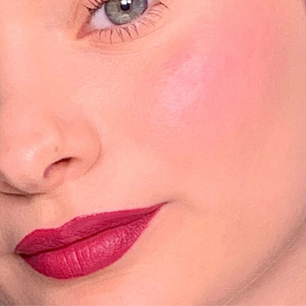 Nahaufnahme eines Gesichts mit rosa Rouge auf den Wangen und Lippenstift auf den Lippen. Helle Haut.