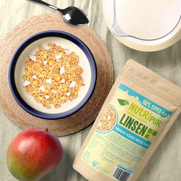 Müsli in Schüssel, Mango, Milchkrug, Löffel und Müsli-Packung. Aufschrift: NutriPur Linsen Mango-Kokos Müsli Mix. Auf hellem Untergrund.
