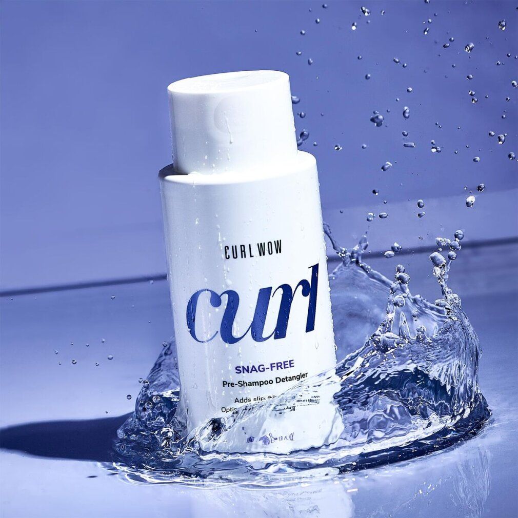 Weiße Flasche, umgeben von Wasserspritzern. Aufschrift: CURL WOW, curl, SNAG-FREE Pre-Shampoo Detangler. Blaue Oberfläche.