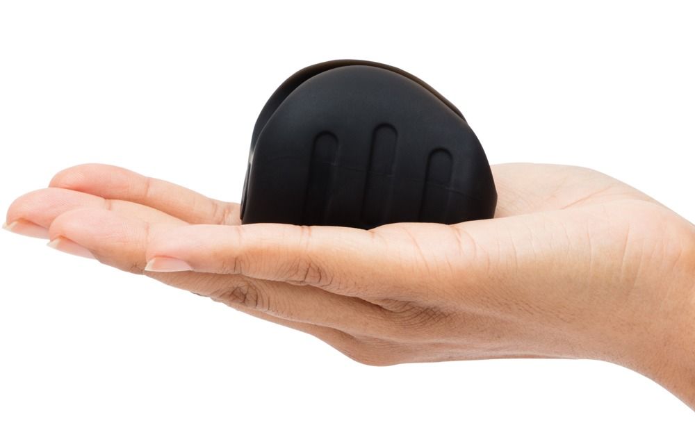 Hand hält schwarzes, ovales Wellness-Produkt mit drei länglichen Rillen.