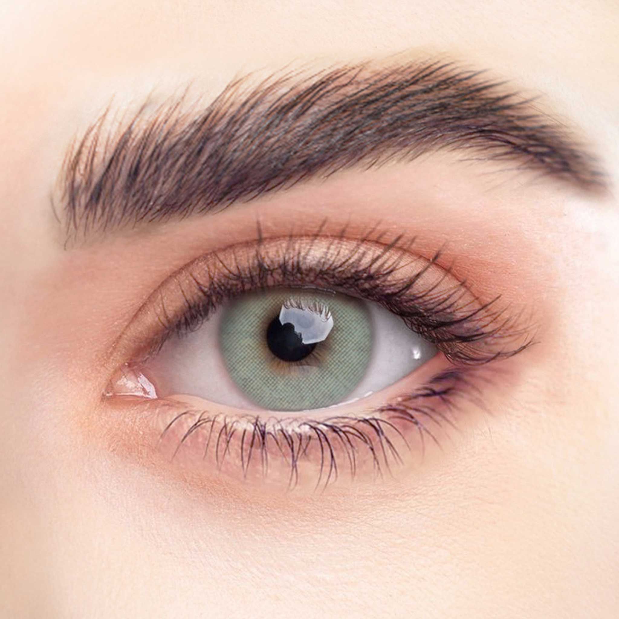 Nahaufnahme eines Auges mit grüner Kontaktlinse. Sichtbare Wimpern und Augenbrauen. Natürlicher Hautton.