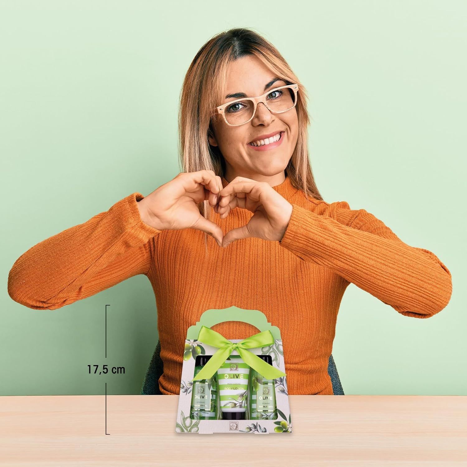 Frau hält Hände herzförmig vor Geschenkbox. Geschenkbox mit Produkten, Schleife und Aufschrift 'OLIVE'.