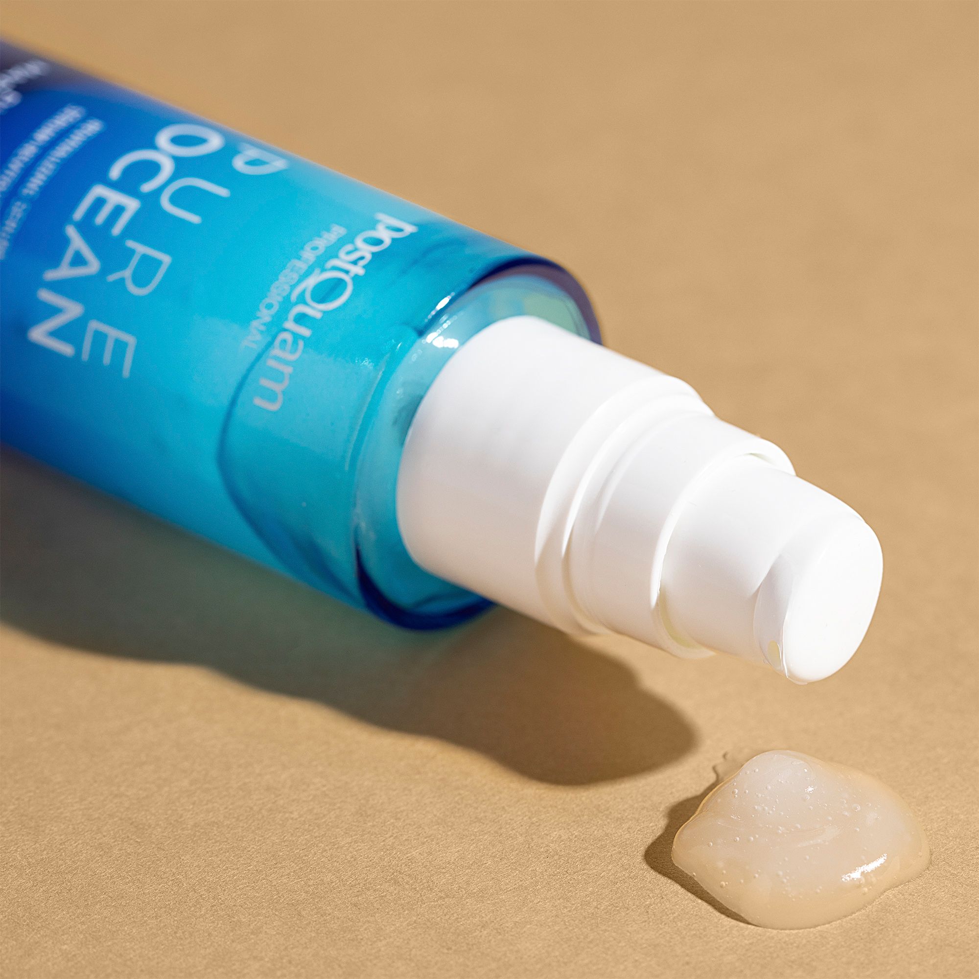 Serumflasche liegt. Aufschrift: Postquam Pure Ocean. Serumtropfen auf beigem Untergrund. Weißer Pumpkopf.